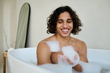 Banyo yaparken köpükle oynayan mutlu ve ışıl ışıl bir adam.