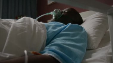 Sağ kolunda damardan damar yolu olan yaşlı bir adamın beyaz çarşafla hastanede baygın yatarken çekilmiş bir fotoğrafı.