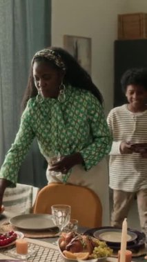 Siyahi genç bir kadının ev kutlama masasını düzenlemesi, oğlunun tabak getirmesi, annenin ona yardım ettiği için teşekkür etmesi dikey bir bakış açısı.