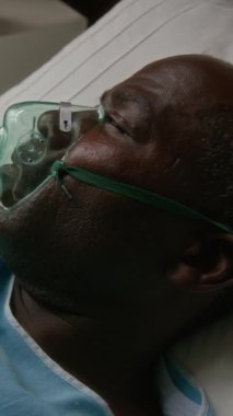 Hastane yatağında yatan, oksijen maskesi takan, nefes almakta zorlanan yaşlı bir adamın dikey yakın çekimi.