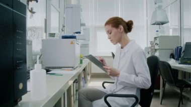 Genç bayan araştırmacının laboratuvar koltuğunda elinde pano tutarken verileri analiz ederken görüntüyü yakınlaştır