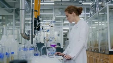 Masada laboratuvar malzemeleriyle bilimsel araştırmalar yaparken beyaz önlüklü genç kadın kimyagerin yan görüntüsü.