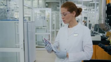 Beyaz önlüklü ciddi bir beyaz kadın araştırmacının belden yukarı portresi. Laboratuvarda bilimsel belgelerle kameraya poz veriyor.