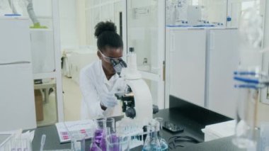 Modern laboratuardaki bilim deneyi için mikroskop ve yazı raporları kullanarak Afrikalı Amerikalı genç kadın biyoloğu yakından çek.