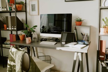 Şifreli büyük bilgisayar ekranı. Bitkiler, ofis malzemeleri, kitaplarla dolu raflar.