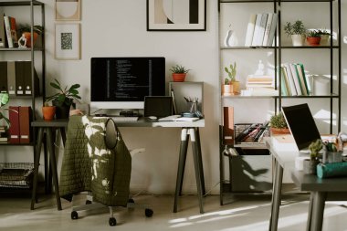 Çalışma masaları, dijital cihazları ve kitap rafları olan boş bir ofis