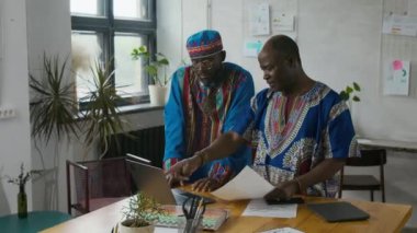 Uyumlu mavi Afrikalı iki adam laptopta veri tartışırken aynı zamanda modern açık çalışma alanında iş projesinde birlikte çalışıyorlar.