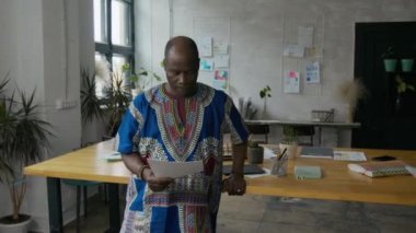 Canlı geleneksel Afrika kıyafetleriyle modern ofis çalışma alanındaki belgeleri tartışan iki siyah adam.