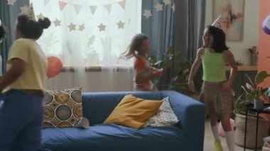 Beş tane çok ırklı çocuk, dekore edilmiş oturma odasında doğum gününü kutlarken kanepenin etrafında koşturuyor.