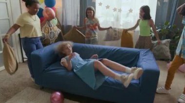 Kanepeye düşen bir kız, dört arkadaş ona yastık fırlatırken çocuklar ev partisinde eğleniyor.