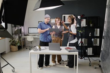 Geniş çerçevede gülümseyen ve çizimlere bakan bir manken. Yaratıcı yönetmen bunu gösteriyor ve detayları anlatıyor. Zarif bir kadın modellerin yüzüne makyaj yapıyor.