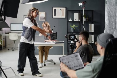 Kameraman kameraya bakarken, kadın sahneyi başlatmak için el çırpıyor.