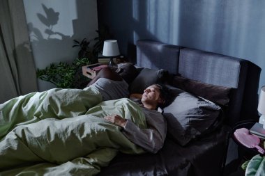 Çift ırklı çiftin rahat bir yatakta rahat uyuduğu yüksek açılı bir çekim. Gece ay ışığıyla çizilmiş.