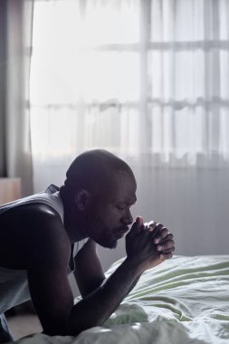 Afro-Amerikan bir adamın yatmadan önce diz çöküp dua edişinin dikey çekimi.