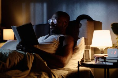 Afrika kökenli Amerikalıların düşük açılı görüntüleri gece geç saatlerde yatak odasında kitap okumaya odaklanmış.