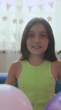 Gen alfa kızının dikey portresi iki balon kusuyor ve doğum günü kutlamalarında kameraya gülümsüyor.