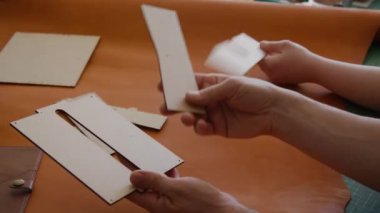 Tanımlanamayan meslektaşlar, dağınık ama düzenli çalışma alanlarına yayılmış büyük kahverengi deri derileri kesmek için küçük desenleri inceliyorlar.