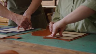 Önlüklü tanınmayan usta bir zanaatkar ve onun iş arkadaşı tentelerle deri kesiyorlar, atölyede ahşap desenler kullanıyorlar.