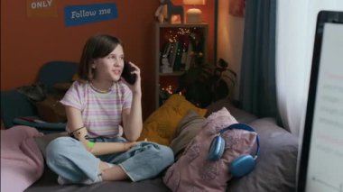 Neşeli genel alfa kız evde boş zamanlarında yatakta dinlenirken sınıf arkadaşıyla telefonda konuşuyor.