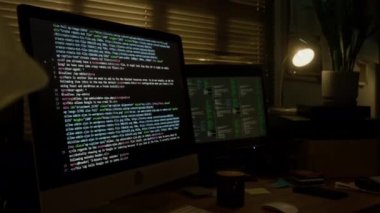 Kısmen kapalı perdeli loş programcı odasında dağınık masa üzerinde iki monitörün görüntülendiği bir görüntü yok.
