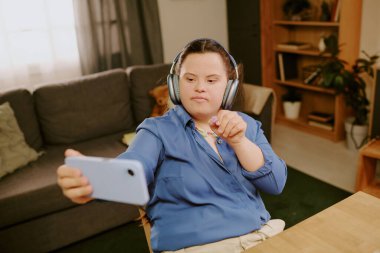 Down sendromlu yaratıcı kızın yüksek açılı görüntüsü akıllı telefondan selfie çekerken çiçek şeklindeki boncuğu gösteriyor.