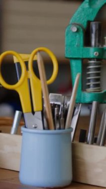 Sarı saplı makas, tahta çubuklar, metal aletler ve deri atölyedeki yeşil metal pres ile dikey yakın çekim küçük konteynır