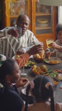 Afro-Amerikan ailesinin dikey görüntüsü, evdeki bayram kutlamaları sırasında yemek masasının etrafında toplandı ve kadeh kaldırdı.