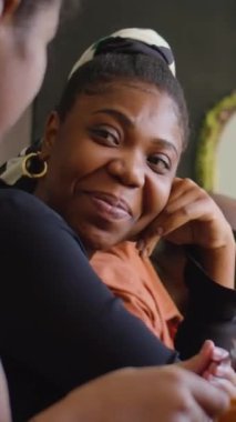 Evdeki aile kutlamaları sırasında yemek masasında oturan, çocukla gülümseyen ve sohbet eden neşeli siyahi kadının dikey çekimi.