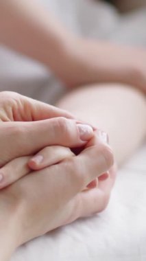 Hastane yatağında yatan hasta bir kadının el ele tutuşup iyileşme sürecinde onu desteklerken çekilmiş dikey yakın çekimi.