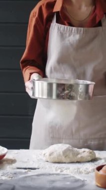 Önlüklü kadın fırıncının ekmek hazırlarken mutfakta hamurun üzerinde un ellerken dikey kesimi.