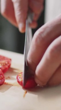 Ahşap kesme tahtasıyla taze kiraz domateslerini kesen tanınmayan şefin dikey yakın çekimi.