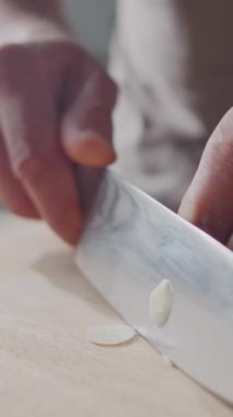 Yemek hazırlarken tahta kesme tahtasıyla taze sarımsak karanfilleri doğrayan bir adamın dikey yakın çekimi.