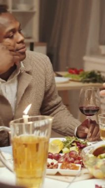 Şenlik masasında yemek yerken kadehleri kaldıran çeşitli genç arkadaşların dikey görüntüsü.