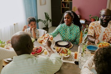 Afro-Amerikan bir ailenin farklı geleneksel yemeklerle masada oturduğu ve şenlikli öğle yemeği yediği yüksek açılı bir fotoğraf.