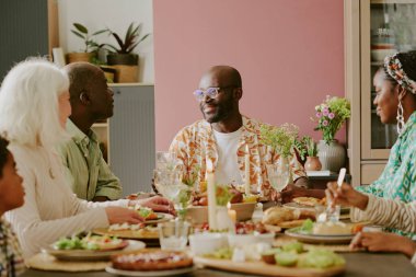 Afrikalı Amerikalı yetişkin bir adam ailesiyle, çocuklarıyla ve sevimli karısıyla yemek yerken babasıyla sohbet ediyor.
