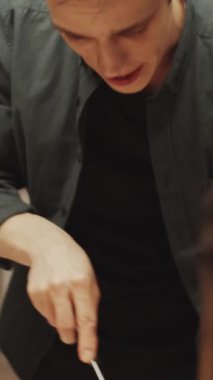 Genç erkek ev sahibinin evde birlikte yemek yerken kızarmış et kesip arkadaşlarının tabağına koyduğu dikey görüntü.