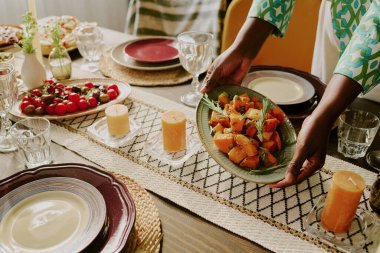 Yüksek açılı, tanınmayan bir kadın eli, elinde biberiyeli fırında tatlı patates tabağı.