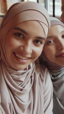 Fotoğraf makinesinde selfie çekerken kameraya poz veren tesettürlü iki genç Müslüman arkadaşın dikey UGC görüntüsü.