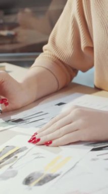 Gözlüklü sarışın kadın terzinin dikey görüntüsü. Stüdyoda erkekler için kıyafet tasarlarken resimlerle çalışıyor.