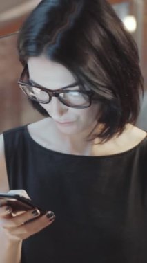 Modern ofisin çalışma saatlerinde camdan duvarları olan akıllı telefondan mesaj yazan esmer ve zarif kadın yöneticinin dikey görüntüsü