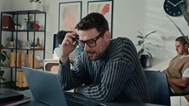 Genç adamın portresi, modern açık uzay ofisinde otururken kameraya bakıp nazikçe gülümsemesi.