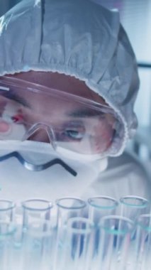 Bilimsel deney sırasında pipet kullanarak test tüpüne mavi solüsyon damlatan kadın laboratuvar teknisyeninin dikey yakın çekim odak çekimi.
