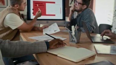 Çeşitli meslektaşlar projelerinin finansal yönetimi hakkında konuşuyor, iş toplantısı sırasında modern ofiste masada oturuyorlar.