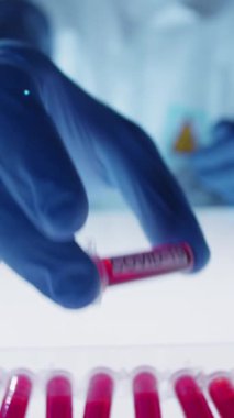 Korunaklı giysiler içindeki bilinmeyen virolojistin dikey yakın çekimi Coronavirus 'a karşı aşı geliştirirken kovid-19 etiketli kan örneğini test tüpleriyle kutuya koyuyor.