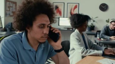 Orta Doğulu kıvırcık saçlı bir adam önemli bir iş görüşmesi yaparken, meslektaşları modern açık uzay ofisinde kendi görevleri için sıkı çalışıyorlar.