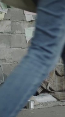 İnsanlar yanından geçerken, siyah erkek sokak dilencisinin karton tabela ve metal bardağın yanında yattığı dikey görüntü.