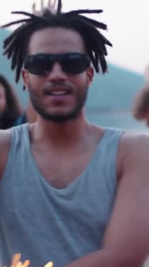 Güneş gözlüklü, gri tişörtlü, maytapla dans eden ve yaz partisinin tadını çıkaran Z jenerasyonunun dikey görüntüsü.