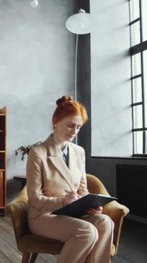 Geniş ofis günlerinde panoya yazılı takım elbise giymiş, beyaz saçlı kadın psikoloğun dikey görüntüsü.