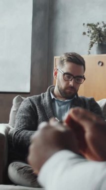 Gözlüklü beyaz erkek terapistin, danışmanlık sırasında duygularını paylaşan tanınmayan siyahi müşteriyi dikkatle dinlerken,