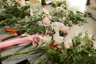 Yüksek açılı pastel güller, yapraklar ve çiçekçinin çalışma masasında saten kurdeleler.